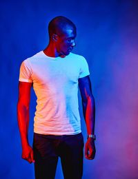 Young man with shaved head standing against colored background