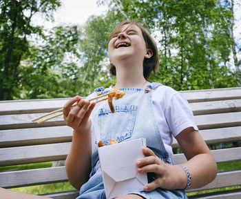 Teenage girl on a walk on a summer day in the park has lunch with noodles wok