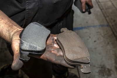 A car mechanic holds in a dirty, open hand a new and old brake pad, visible brake lining of pads.