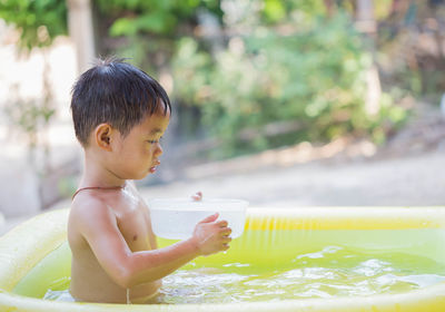 Shirtless boy playing with container in wading pool