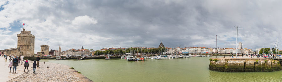 Panoramic view of buildings by sea against cloudy sky