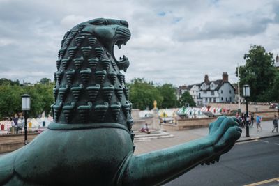 Gargoyle in city against cloudy sky