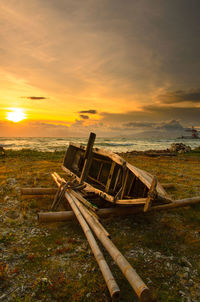 Abandoned boat on land against sky during sunset