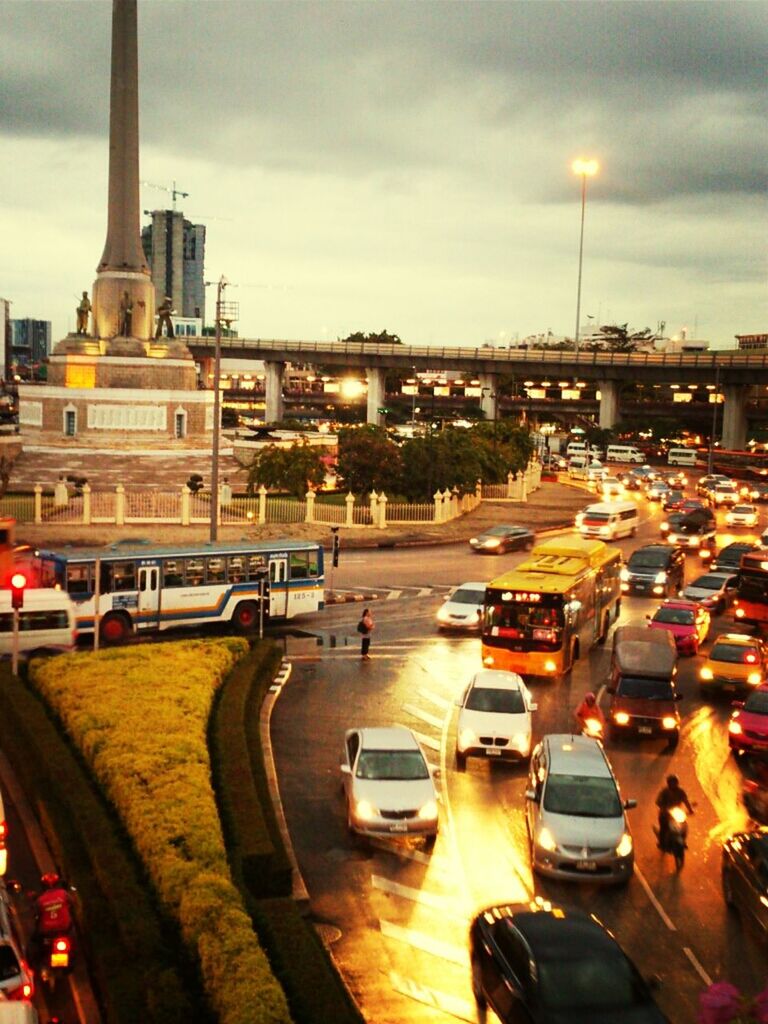 transportation, car, land vehicle, mode of transport, city, architecture, building exterior, street, built structure, traffic, sky, road, street light, cloud - sky, illuminated, on the move, city street, city life, travel, sunset