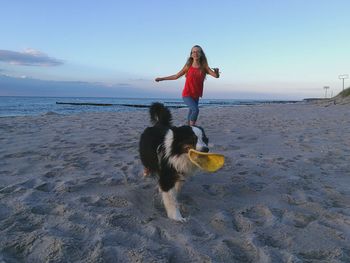 Portrait of young woman with dog standing on beach against sky