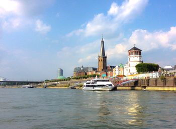 Nautical vessel on river by buildings in city against sky