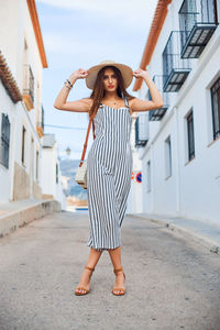 Full length portrait of young woman standing against building