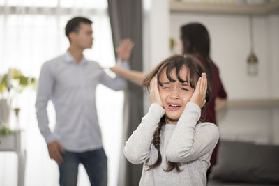 Close-up of girl crying while parents fighting in background at home