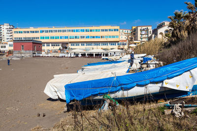 Deck chairs on beach by buildings against blue sky