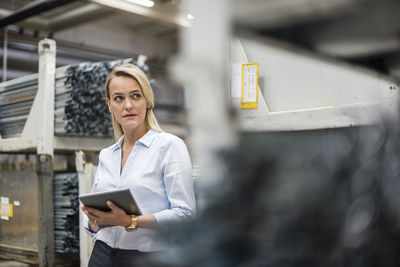 Blond woman holding tablet in high rack warehouse
