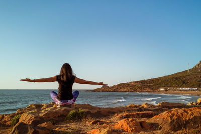 Rear view of woman on rock in sea against clear sky