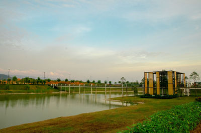 Building by river against sky during sunset