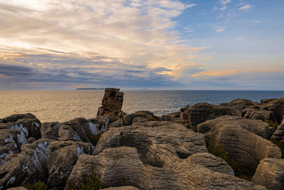 Rocks by sea against sky during sunset