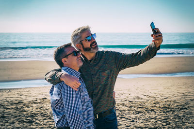 Mature man friends taking selfie while standing at beach