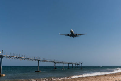 Airplane flying over sea against clear blue sky