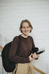 Portrait of happy young woman with backpack and folder in university