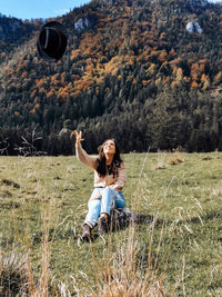 Young woman sitting on grass in valley, throwing hat in air, autumn, fall, happy.