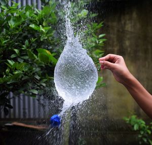 Cropped hand of person breaking water balloon against plants 