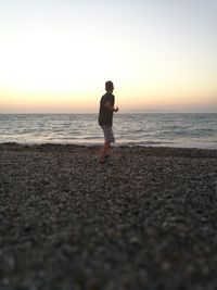 Full length of man standing on beach against sky during sunset