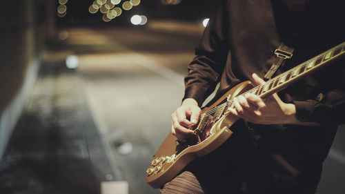 Midsection of man playing guitar on footpath at night