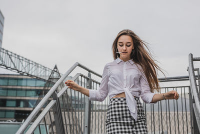 Young woman standing on staircase against sky