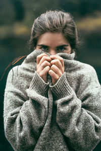 Portrait of young woman covering face with comfy sweater