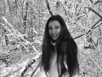 Portrait of smiling young woman standing in frozen forest