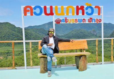 Portrait of man sitting on wooden seat against landscape