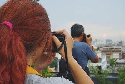 Rear view of woman photographing man against sky