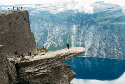 People on cliff by lake against mountains