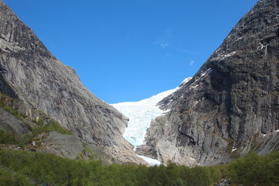 Low angle view of rocky mountains against clear blue sky