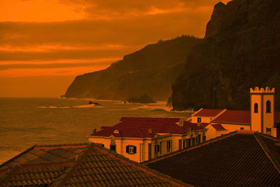 Houses by sea against sky during sunset