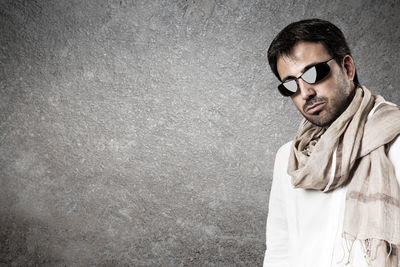 Young man wearing sunglasses standing against wall