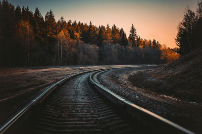 Railroad tracks by trees against sky during sunset