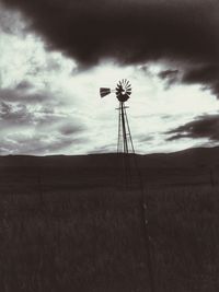 Silhouette of windmill on field against cloudy sky