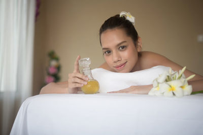 Portrait of smiling young woman with oil lying on massage table in spa