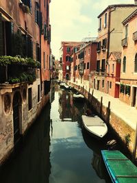 Boats moored in canal amidst buildings against sky