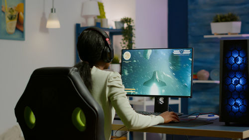 Rear view of woman playing game on desktop computer