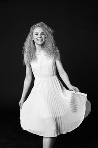 Portrait of a smiling young woman standing against black background