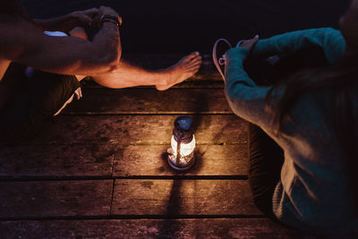 High angle view of couple sitting around illuminated lantern on pier