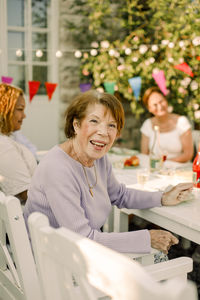 Portrait of happy elderly woman sitting at dining table in back yard