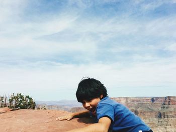 Side view of boy climbing mountain against cloudy sky during sunny day