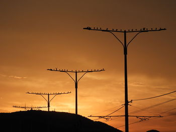 Low angle view of silhouette electricity pylon against sky during sunset
