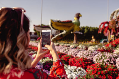 Close-up of young woman taking picture on mobile phone in ornamental garden