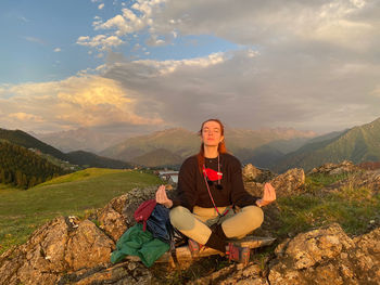 Full length of man sitting on mountain against sky