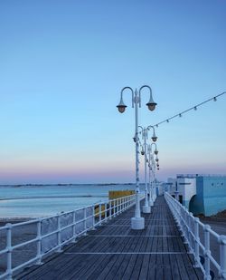 Street light by sea against clear blue sky