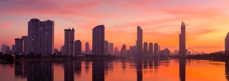 Reflection of buildings in city against sky during sunset