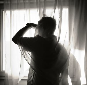 Rear view of woman standing by window at home