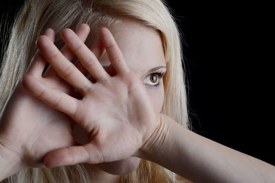 Close-up of young woman covering face against black background