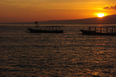Silhouette boat in sea against orange sunset sky